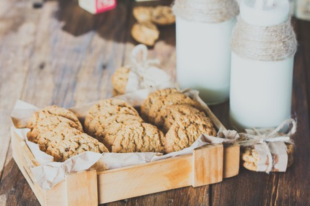 School milk bottles and oatmeal cookies on wooden background. Toningの写真素材