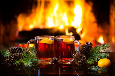 Christmas New Year composition. Two glasses of mulled red wine or hot drink tea with christmas decoration - fir branches in front of warm fireplace. Romantic, relaxed magical atmosphere near fireplaceの写真素材