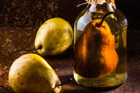 Traditional Chilean pear brandy with whole pear inside bottle. Aguardiente de pera. Bottle of pear aguardiente brandy and fresh pear on rustic dark background. Latin American drinkの写真素材
