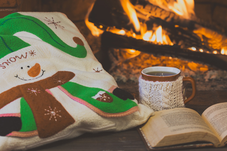 Antigue books, tea hot drink in mug, pillow with Christmas decor near fireplace. Fireplace as background. Christmas or winter concept.の写真素材