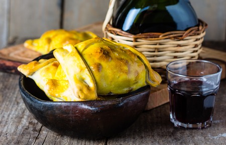 Empanadas. Latin American chilean food. Typical traditional Chilean empanadas with meat, onion, eggs and olives on mapuche rustic cutting board, two glasses and bottle of red wineの写真素材