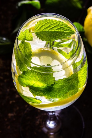 Glass of alcohol cocktail or lemonade. Mohito cocktail with lemon, mint, ise cubes. Cold drink. Fresh lemons and mint on wooden backgroundの写真素材