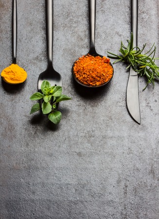 Food background with fresh herbs - rosemary and oregano, dryed spices - chili pepper, turmeric curcuma and black steel cutlery - knife spoon fork, tea spoon on black background. Top view. Copy spaceの写真素材