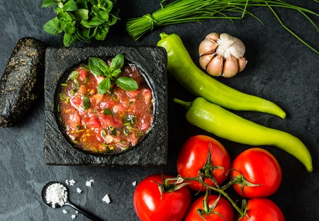 Traditional Latin American mexican Tomato sauce salsa, chilean chancho en piedra in stone mortar and ingredients tomatoes, chile, garlic, onion, sea salt on dark slate stone background. Top viewの写真素材