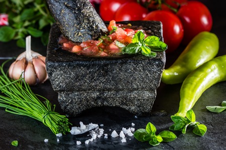 Traditional Latin American mexican Tomato sauce salsa, chilean chancho en piedra in stone mortar and ingredients tomatoes, chile, garlic, onion, sea salt on dark slate stone backgroundの写真素材