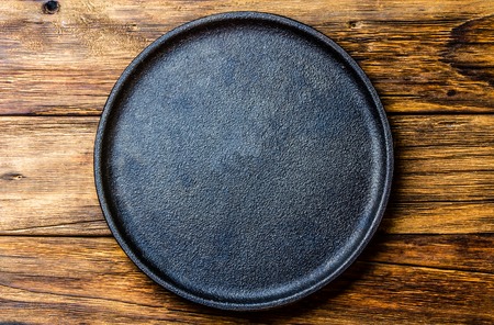 Empty rustic black cast iron plate over old wooden background. Top viewの写真素材