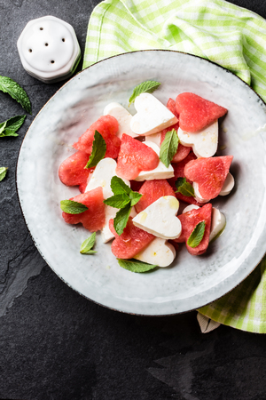 Mediterranean Italian Salad with watermelon and cheese feta cut as hearts and mint on grey plate on slate background. Valentine day menu consept. healthy food. Top viewの写真素材