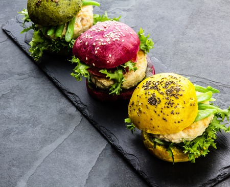 Colored green, yellow and purple burgers on slate board. Top viewの写真素材