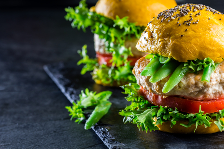 Colored yellow burgers. Homemade American chicken burgers hamburgers with turmeric curcuma and chia buns and vegetables. Trendy food. Close up, slate background.の写真素材