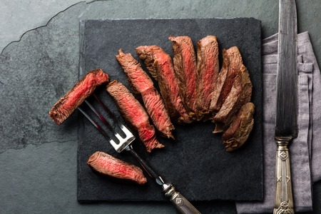 Medium rare beef steak on slate board, vintage cutlery, grey backgroundの写真素材
