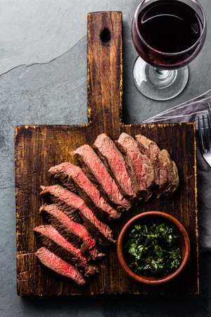 Slices of beef medium rare steak on wooden board, glass of red wine on slate backgroundの写真素材