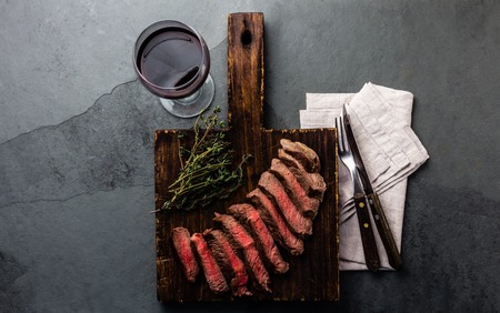 Slices of beef medium rare steak on wooden board, glass of red wine on slate backgroundの写真素材