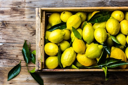 Box of lemons with fresh leaves on wooden background with copy space. Top viewの写真素材