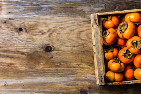 Box of fresh fruits persimmon kaki on wooden background. Copy spaceの写真素材