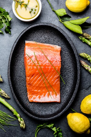 Raw salmon fillet. Asparagus, lemons, olive oil and herbs around plate with salmon. Food cooking background. Top viewの写真素材