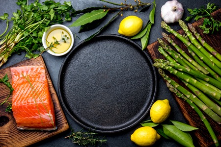 Raw salmon fillet, asparagus, lemons and herbs around cast iron plate. Food cooking background with copy space. Top viewの写真素材