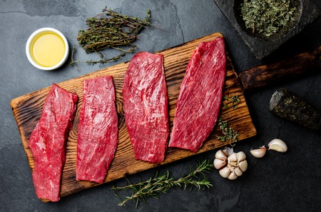 Fresh raw meat beef steaks. Beef tenderloin on wooden board, spices, herbs, oil on slate gray background. Food cooking background concept.の写真素材