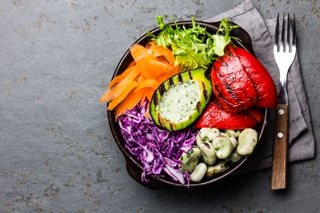 Budha bowl. Raw vegetables with beans, grilled avocado and bell pepper on slate backgroundの写真素材