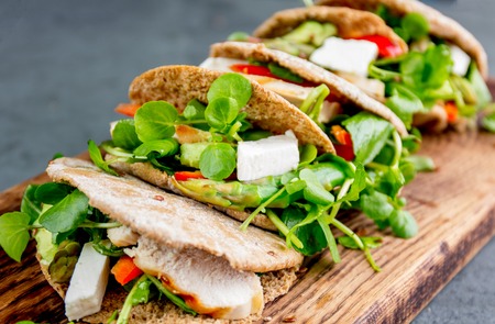 Pita sandwiches stuffed with chicken, vegetables and cheese on wooden cutting board.の写真素材