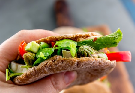 Hand holding vegetarian pita sandwich stuffed with asparagus, bell pepper, avocado and fresh leaves.の写真素材