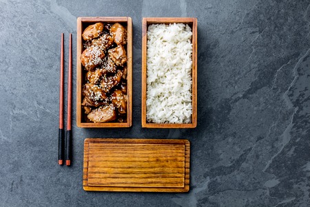 Japanese food. Chicken teriyaki with rice in wooden bento lunch box. slate background, top viewの写真素材