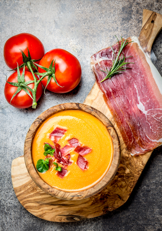 Spanish tomato soup Salmorejo served in olive wooden bowl with ham jamon serrano on stone background. Top view.の写真素材