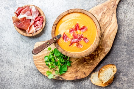 Spanish tomato soup Salmorejo served in olive wooden bowl with ham jamon serrano on stone background. Top view.の写真素材