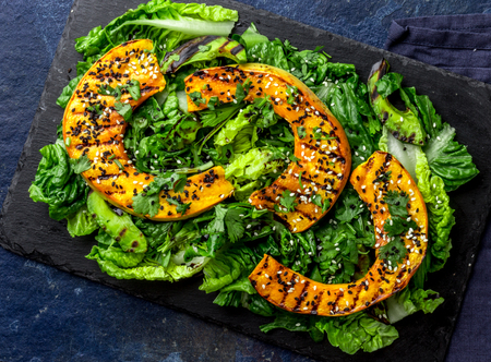 Grilled pumpkin and lettuche salad with white and black sesame and balsamic sauce on slate black board, blue stone backgroundの写真素材