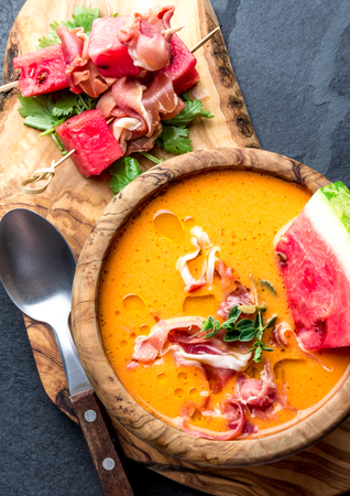 Salmorejo soup with watermelon. Traditional spanish cold tomato soup with watermelon and ham serrano in olive wooden bowl, slate background, top viewの写真素材
