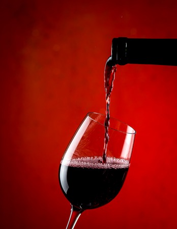 Pouring red wine into a glass, red backgroundの写真素材