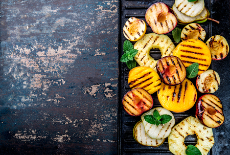 GRILLED FRUITS. Grill fruits - pineapple, peaches, plums, avocado, pear on black cast iron grill board. Copy spaceの写真素材