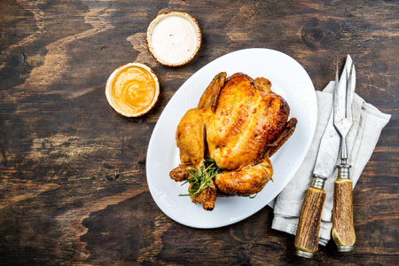 Roasted chicken with rosemary served on white plate with sauces on wooden table, top view.の写真素材