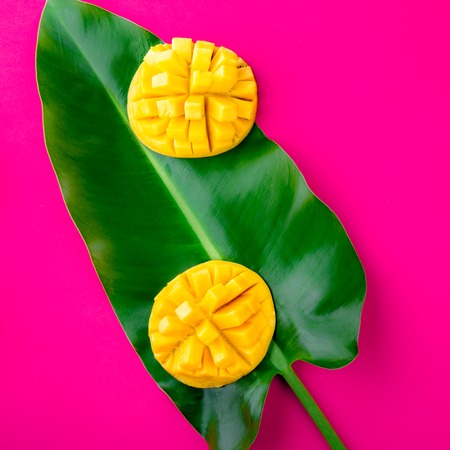 Creative layout made of summer tropical fruits mango and tropical leaves on pink background. Flat...