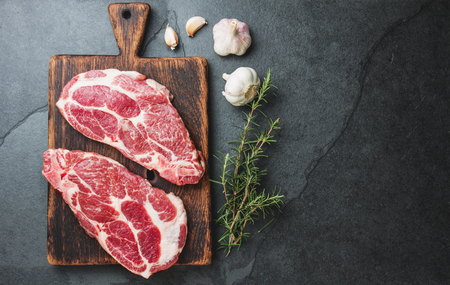 Raw pork steaks with seasoning on wooden board. Gray slate background.の写真素材