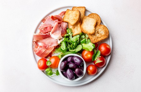 Antipasto Plate with dried bread, ham serrano, tomato cherry and purple olives. White backgroundの写真素材