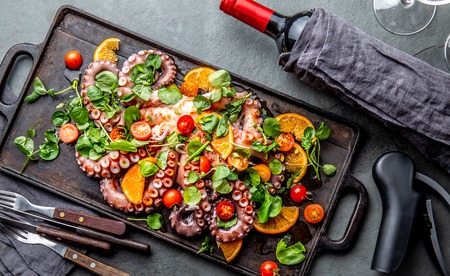 Whole octopus salad with orange, tomatoes and cress salad served on board with wineの写真素材