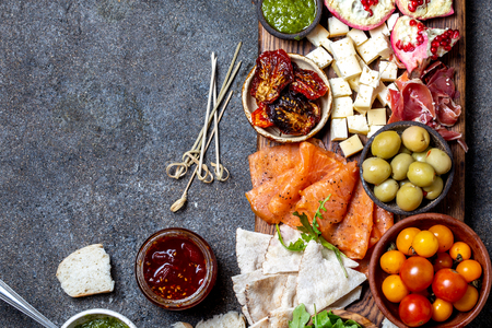 Antipasto. Wine set appetizer. Ham serrano, smoked salmon, dried and fresh tomatoes olive cheese, wine on board. Top view, gray cncrete background.の写真素材