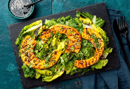 Grilled pumpkin salad with lettuce on black board plate, blue slate background. Autumn menu. Top viewの写真素材