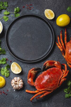 Food background with empty black plate, fresh crabs, lemons and herbs. Top view, copy spaceの写真素材