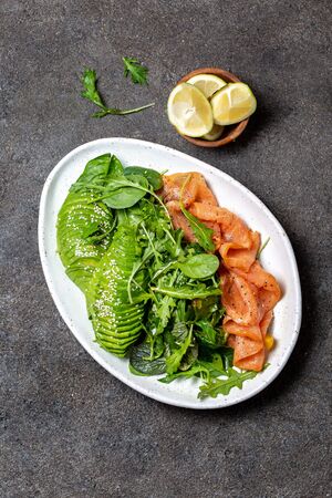 Low carbs salad. Spinach, rucola salad with avocado and salmon. Black concrete background, top view.の写真素材