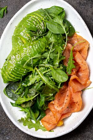 Low carbs salad. Spinach, rucola salad with avocado and salmon. Black concrete background, top view.の写真素材