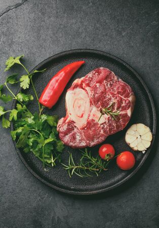 Raw fresh ossobuco con herbs, garlic and chile pepper on black plate. Dark background.の写真素材