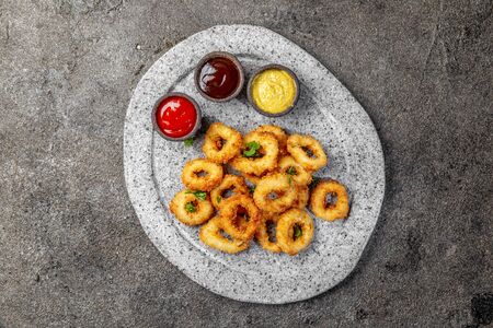 Fried squids rings on gray stone plate with sauces. Gray concrete background.の写真素材