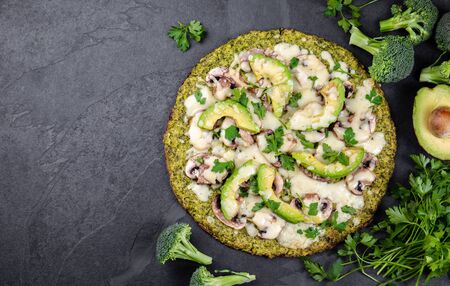 Green broccoli dough crust pizza with avocado, cheese. Low carbs, diet vegan vegetarian pizza on slate background top viewの写真素材