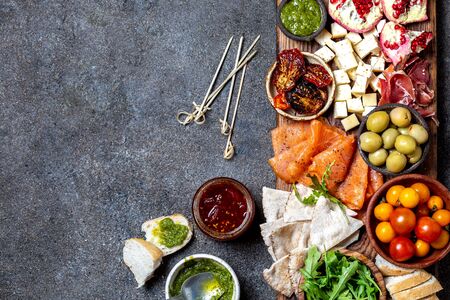 Antipasto. Wine set appetizer. Ham serrano, smoked salmon, dried and fresh tomatoes olive cheese, wine on board. Top view, gray background.の写真素材