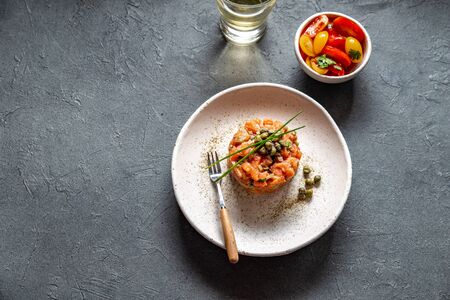 SALMON TARTAR with capers and purple onion on white plate, gray background.の写真素材