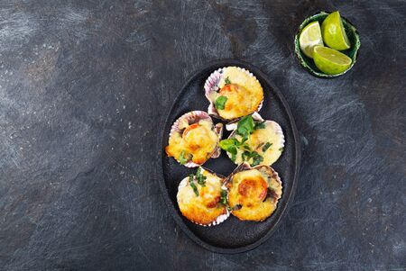 Baked seafood shellfish scallops with cheese and lemon. black background.