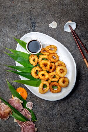 Fried squids rings on white plate decorated with tropical leaves, gray concrete background, top viewの写真素材