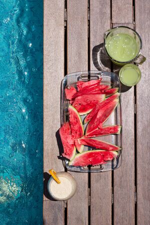 Watermelon plate and summer dkinks near pool. Exotic summer diet. Tropical beach lifestyle.