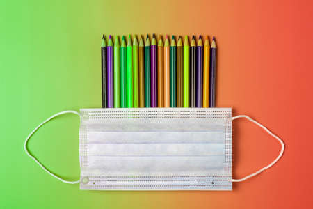 School creative concept in context of pandemic Covid-19. Color pencils and medical mask on colored backgroundの写真素材